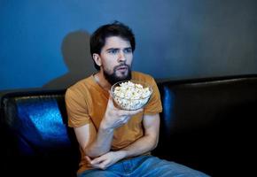 une homme dans le soir avec une assiette de pop corn sur une cuir canapé photo
