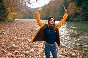 de bonne humeur femme dans une Jaune veste près le rivière l'automne marcher photo