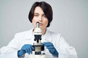 de bonne humeur femelle laboratoire assistant dans blanc manteau microscope professionnel science expériences photo