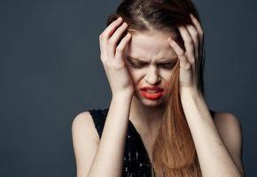 femme dans noir robe émouvant visage avec mains et rouge à lèvres stress irritabilité photo