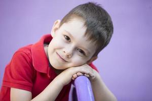 six année vieux garçon. primaire école étudiant. enfant d'âge préscolaire. enfant sur une violet Contexte. aux yeux bruns garçon dans une rouge T-shirt. photo