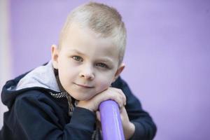 six année vieux garçon. primaire école étudiant. enfant d'âge préscolaire. enfant sur une violet Contexte. peu blond garçon sourit. photo