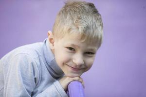 .six année vieux garçon. primaire école étudiant. enfant d'âge préscolaire. enfant sur une violet Contexte. peu blond garçon sourit. photo