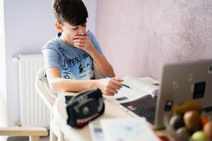 fatigué et somnolent étudiant bâille. Jeune adolescent garçon ayant vidéo conférence appel avec élève en utilisant webcam. en ligne éducation et e-learning concept. Accueil quarantaine distance apprentissage. photo