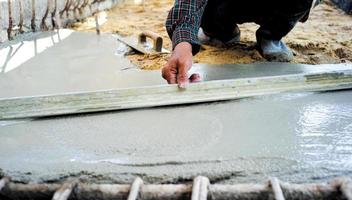 Travailleur à l'aide d'une truelle en bois pour niveler le sol en béton photo