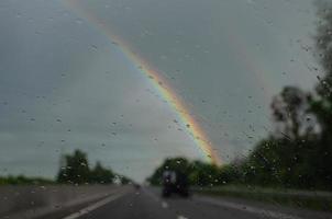 floue vue de le voiture fenêtre sur une arc en ciel dans le pluie photo