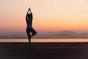 plein longueur arrière vue de femme permanent sur un jambe tandis que Faire yoga à lever du soleil. photo