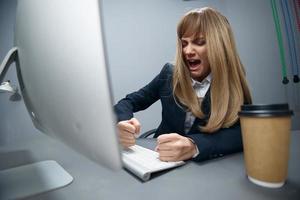 mal irrité millénaire blond femme d'affaires ouvrier dans bleu veste pauses clavier haine opération crash dans gris moderne bureau. éloigné emploi, La technologie et carrière profession concept. large angle photo