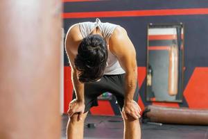 fatigué homme ayant du repos après entraînement. Jeune athlétique homme dans tenue de sport à la recherche épuisé tandis que permanent à Gym photo