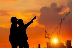 silhouette d'ingénieur et de travailleur vérifiant le projet sur le fond du chantier, chantier de construction au coucher du soleil le soir photo