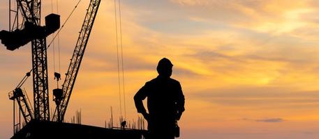 silhouette de ingénieur homme vérification projet à bâtiment site arrière-plan, construction site à le coucher du soleil dans soir temps photo
