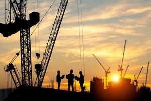 silhouette de ingénieur et ouvrier équipe sur bâtiment placer, construction site à le coucher du soleil dans soir temps photo