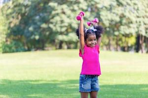 content enfant fille exercice avec haltère dans parc. actif enfant en jouant Extérieur dans le parc photo