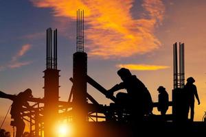 silhouette d'ingénieur et de travailleur vérifiant le projet sur le fond du chantier, chantier de construction au coucher du soleil le soir photo