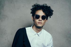 Beau gars avec frisé cheveux dans une blanc chemise et veste sur une gris Contexte la photographie studio portrait photo