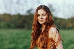 une femme sourit et est content dans la nature dans une vert parc, regards à le le coucher du soleil et sourit. en bonne santé mode de vie concept photo