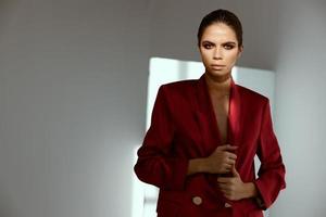 élégant femme dans une rouge veste posant contre une foncé Contexte chute lumière de le fenêtre photo