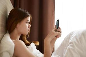 femme avec téléphone dans main dans lit près le fenêtre, rideau photo