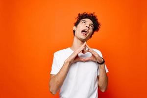 frisé gars dans une blanc T-shirt faire des gestes avec le sien main sur un Orange Contexte photo