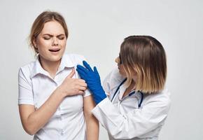 une infirmière dans bleu gants examine une patient dans une blanc T-shirt sur une lumière Contexte photo