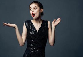 une femme dans une noir robe gestes avec sa mains surprise délice émotions. photo