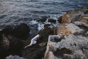 sensuel femme dans une isolé place sur une sauvage rocheux côte dans une blanc robe vue de au dessus photo