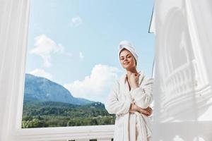 portrait de magnifique femme avec une serviette sur mon tête dans une blanc peignoir de bain rester sur le balcon dans une Hôtel mode de vie photo