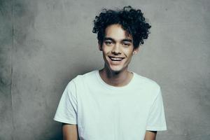 gars avec frisé cheveux dans une blanc T-shirt est assis sur chaises studio photo