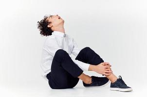 une adolescent dans une costume et baskets est assis sur le sol dans une brillant pièce côté vue photo