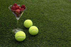 verre de des fraises et tennis des balles sur herbe. photo