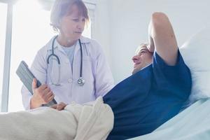 le médecin est examiner le patient dans le hôpital. caucasien femelle médecin parlant à Masculin patient mensonge dans hôpital lit. photo