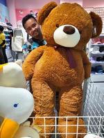 bekasi, Indonésie - 12 mars 2023 un asiatique homme est en portant une gros nounours ours dans une magasin dans résumécon centre commercial bekasi photo