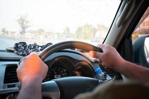 fermer de une homme conduite une voiture avec le sien mains sur le pilotage roue. photo