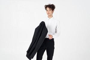 à la mode gars dans une classique costume avec une veste dans le sien main sur une lumière Contexte et frisé cheveux coiffure modèle photo