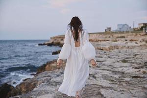femme en marchant dans blanc robe sur pierre plage photo