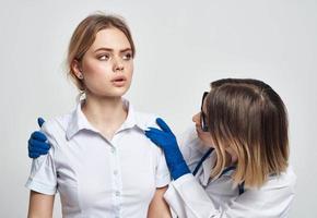 une infirmière dans bleu gants examine une patient dans une blanc T-shirt sur une lumière Contexte photo