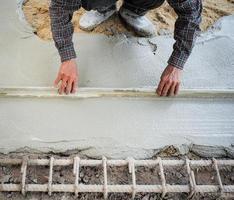 Travailleur à l'aide d'une truelle en bois pour niveler le sol en béton photo