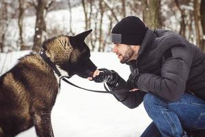 Un homme dans une veste et un bonnet tricoté se promène avec un chien akita américain photo