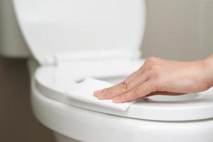 femme en utilisant tissu papier nettoyer le toilette dans le salle de bains à maison. photo