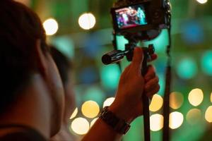 Homme de mouvement flou à l'aide de l'appareil photo avec trépied avec des lumières bokeh étincelantes en arrière-plan