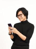 en portant et en utilisant téléphone intelligent avec souriant visage de Beau asiatique homme isolé sur blanc Contexte photo