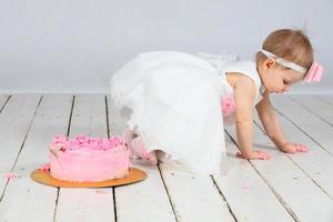 premier anniversaire. peu fille avec une de fête rose gâteau. photo