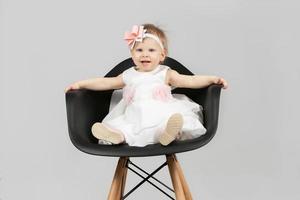 le enfant est un année vieux. magnifique peu fille est séance sur une chaise. marrant enfant avec une arc. mise en charge bébé. photo