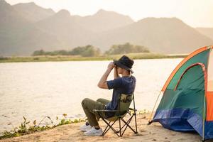 homme camping touristique avec jumelles séance sur le sable plage près touristique tente photo