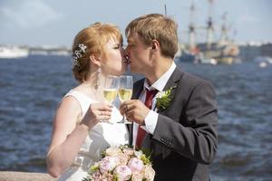 le la mariée et jeune marié avec des lunettes de Champagne contre le Contexte de le rivière. photo