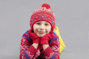 joyeux enfant dans hiver vêtements sur une gris Contexte. garçon dans une rouge tricoté chapeau. à la mode garçon dans le studio sur une gris Contexte. photo