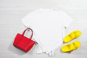 blanc femelle t chemise moquer en haut plat allonger sur en bois Contexte. été accessoires. Jaune retourner flops, rouge sac. Haut de face vue T-shirt copie espace. maquette T-shirt heure d'été. modèle Vide chemise. photo