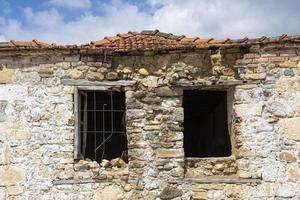 le fenêtre de un vieux pierre maison avec une cassé fenêtre dans le premier plan, ruines de un vieux maison dans le village. photo