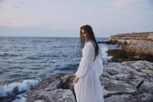 femme dans blanc robe et promenade le long de le océans pierre plage photo