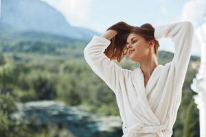 jolie femme longue cheveux dans une blanc peignoir de bain rester sur le balcon dans une Hôtel parfait ensoleillé Matin photo